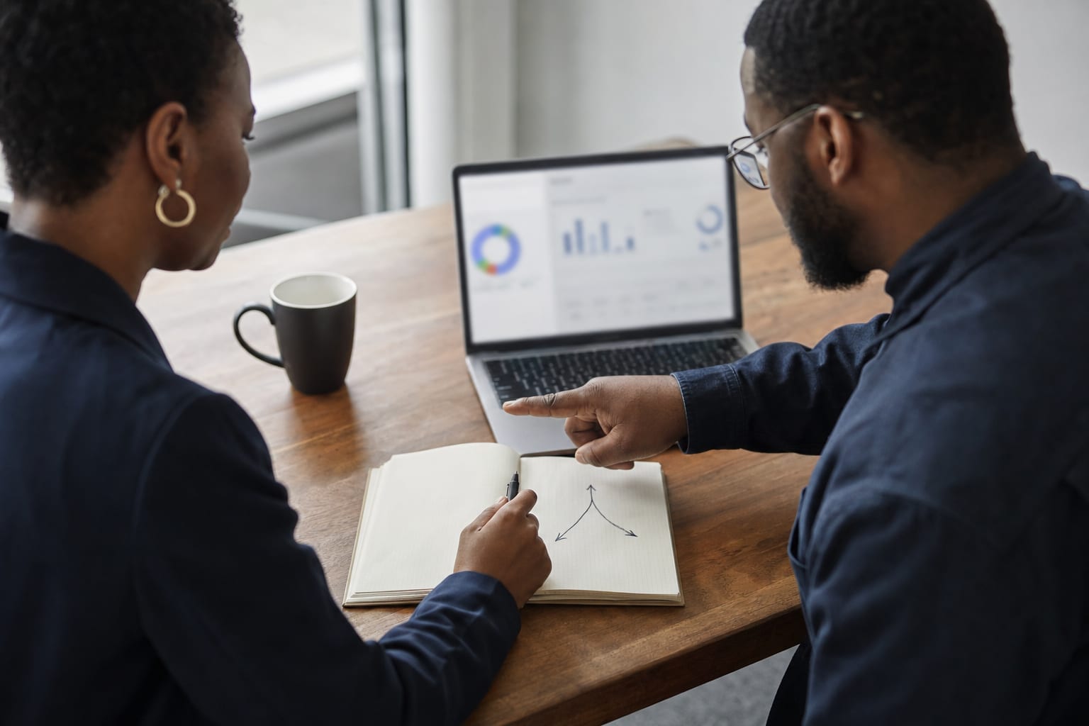 A Black business owner and strategist discussing performance beside an intentionally out-of-focus dashboard.